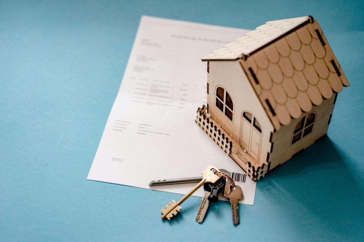 Casa in legno in miniatura con chiavi e contratto appoggiati su un tavolo.